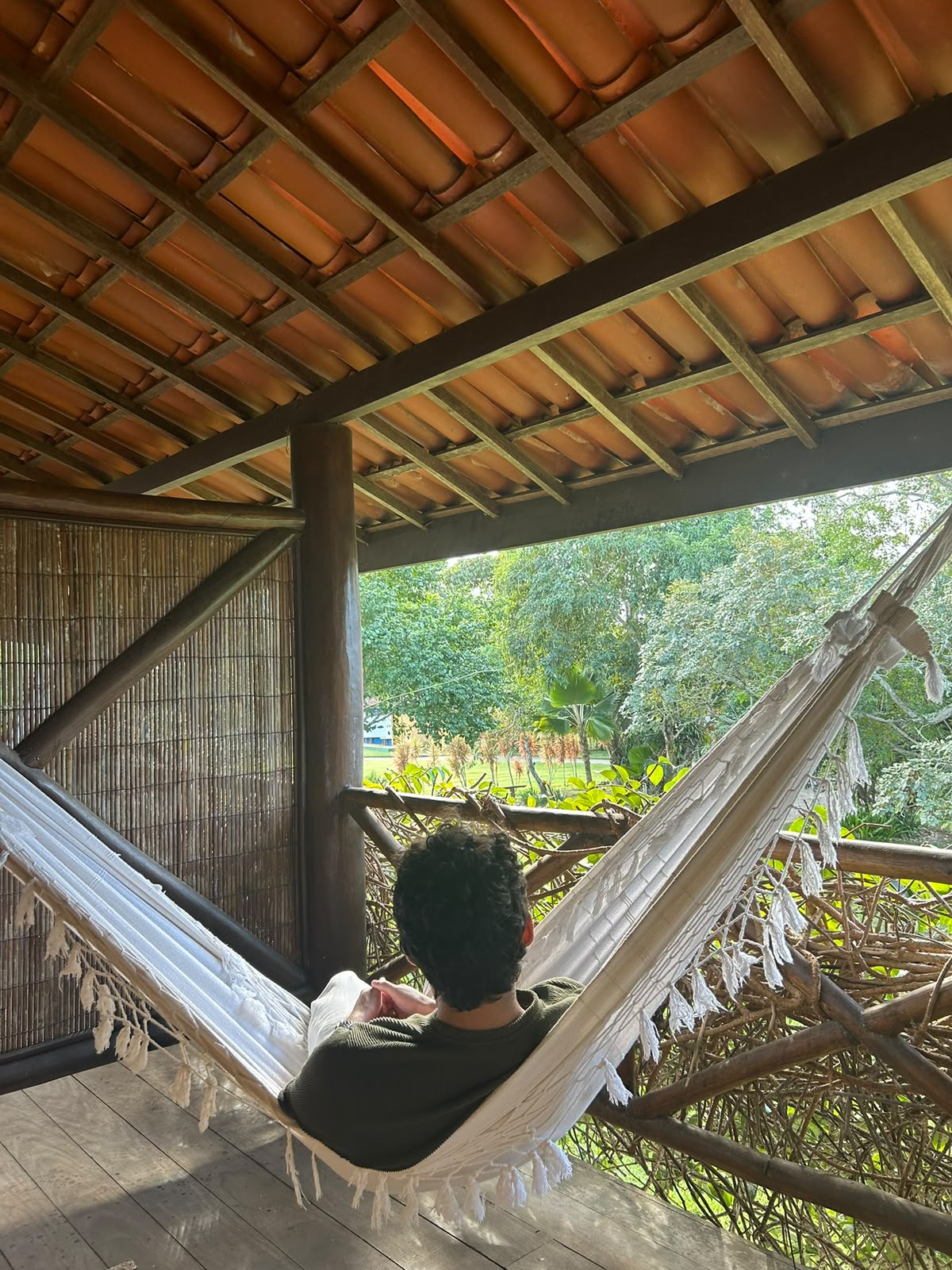 Eduardo descansando em uma rede na varanda de uma pousada cercada pela vegetação.